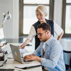 A man and woman collaborating on a project in a modern office with a laptop.
